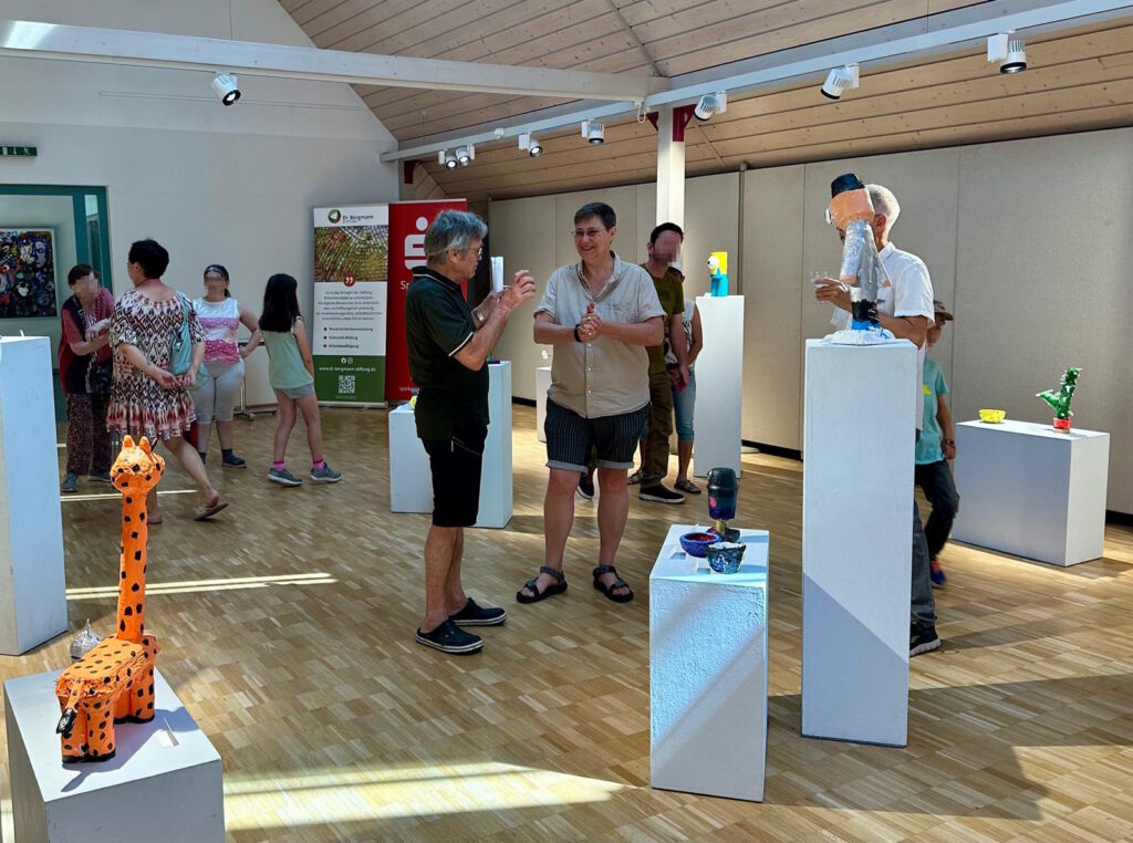 Besucher sprechen miteinander oder laufen durch den Raum der Ausstellung "Wir recyceln Plastikmüll zu Skulpturen".