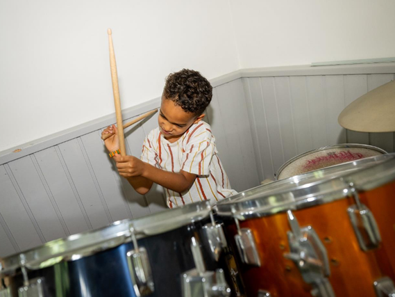 Ein junge übt sich an den Drums und trommelt darauf.